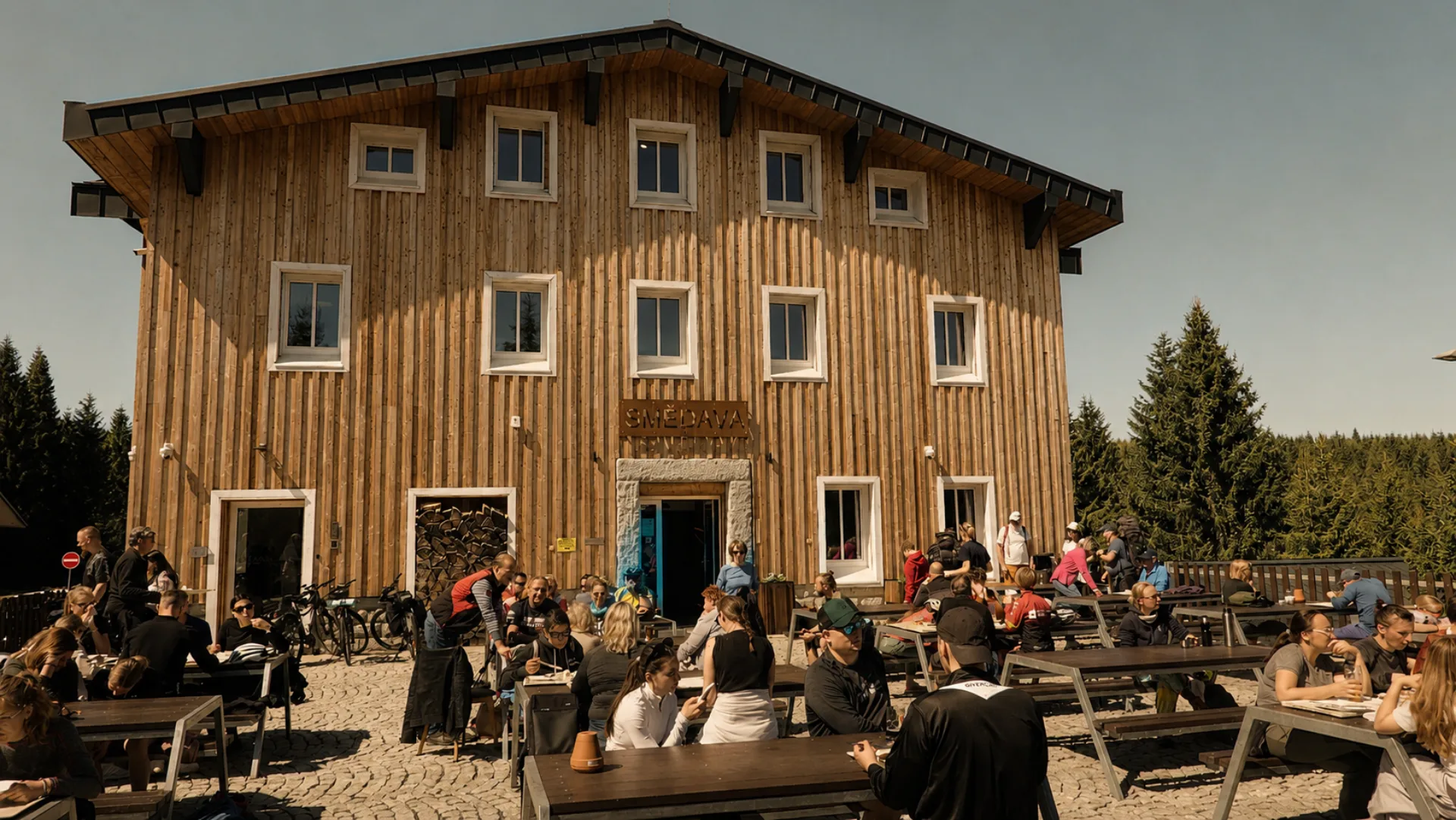 Letní terasa restaurace Horské chaty Smědava plná turistů, cyklistů a návštěvníků odpočívajících v srdci Jizerských hor.