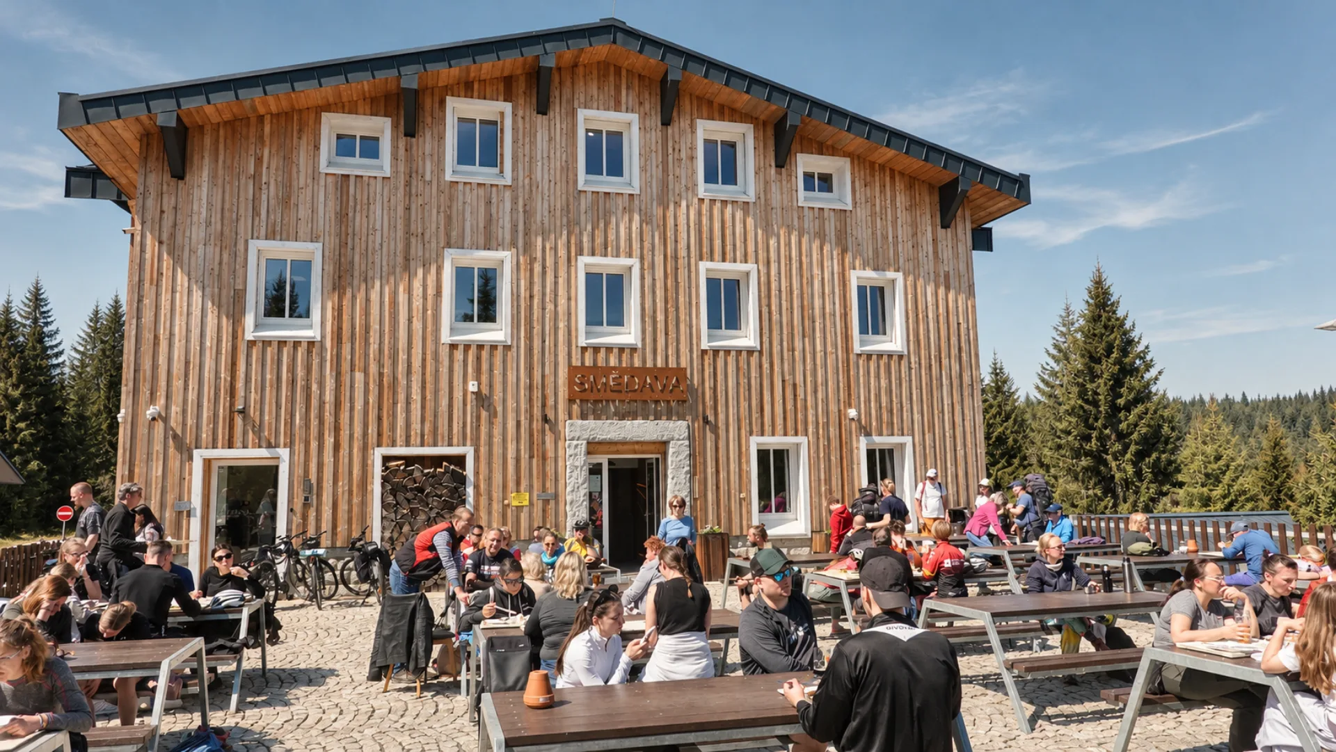 Letní terasa restaurace Smědava s návštěvníky před horskou chatou v Jizerských horách.