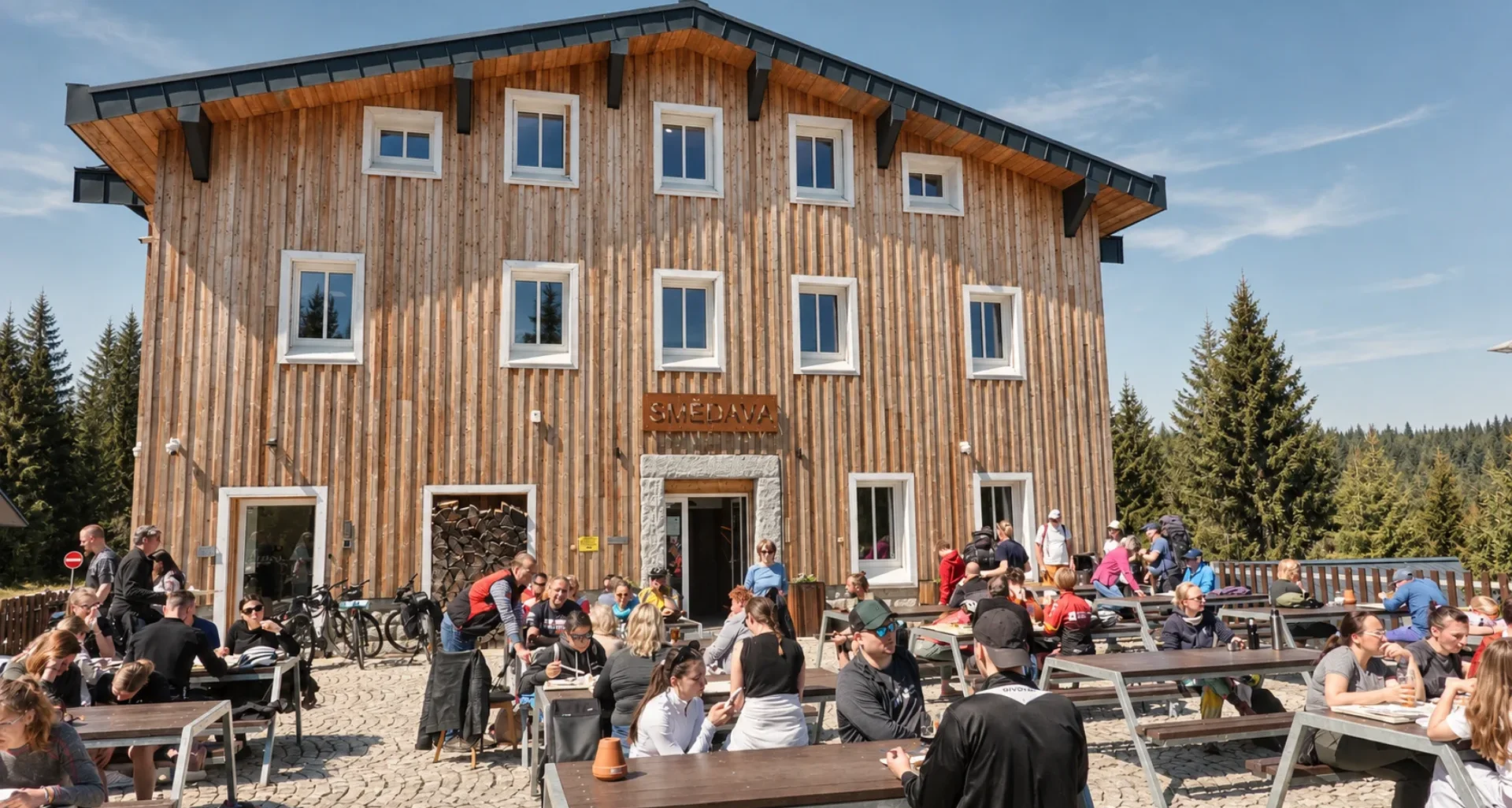 Letní terasa restaurace Smědava s návštěvníky před horskou chatou v Jizerských horách.